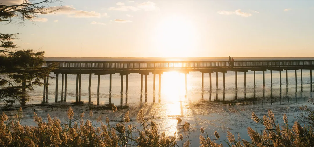 A couple walks down a long peer during sunset at a North Carolina beach.